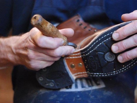 Een personeelslid repareerd een schoen met de hand in de Schoenmakerij van Enschede